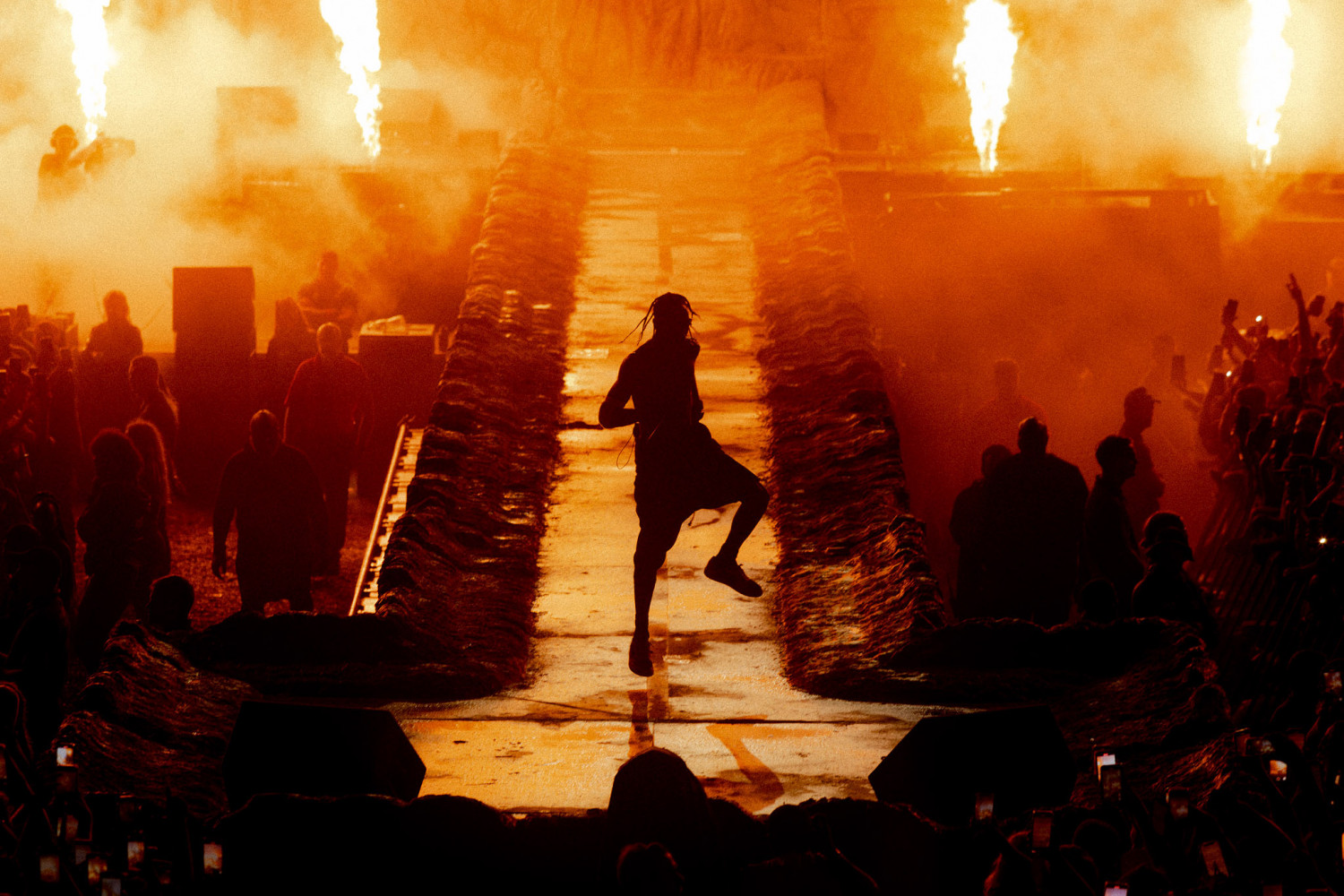 This image is rapper Travis Scott jumping up and down with pillars of fire behind him.